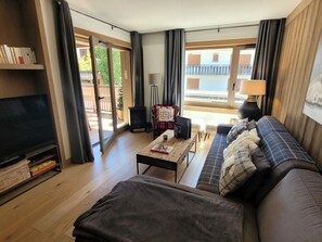 A modern living room with a sofa, a flat-screen TV, a coffee table, and a fireplace. - Beautiful bright apartment in the center, with parking (Les Gets)