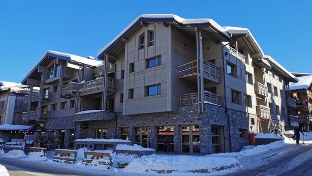 A multi-story hotel with balconies, stone facade, and outdoor seating areas. - Beautiful bright apartment in the center, with parking (Les Gets)