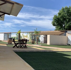 Un patio con una mesa y sillas, césped y un edificio con tejado de tejas.