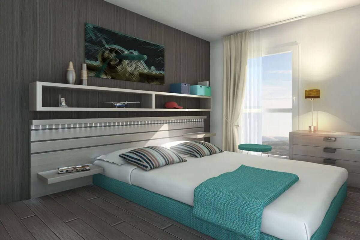 A modern hotel room with a large bed, a built-in wardrobe, a bedside table, a window with curtains, and a city view.