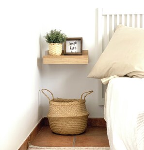 A bedroom with a white bed, a beige pillow, a woven basket, a small potted plant, and a framed sign saying "Laugh love life".