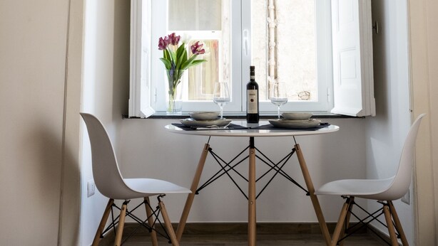 Un coin repas comprenant une table et deux chaises, un luminaire suspendu et une fenêtre donnant sur un mur de pierre extérieur.