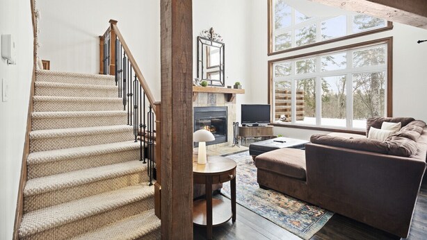 A spacious living room with a large window, a fireplace, a sofa, and a staircase.