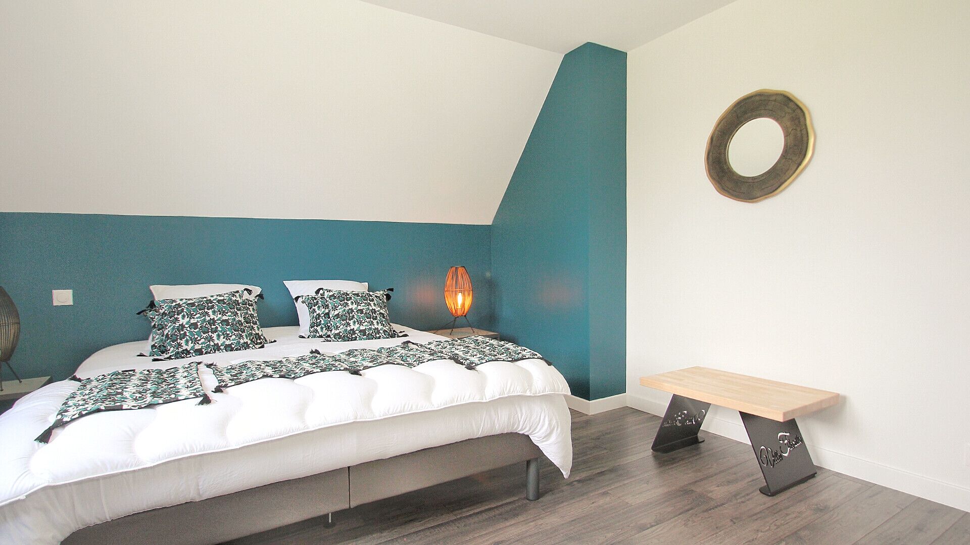 A bedroom with a bed, a bench, a wall-mounted lamp, and a circular decoration.