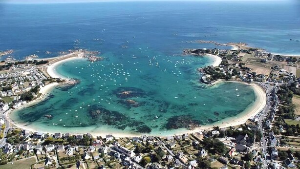 Eine Luftaufnahme einer Küstenstadt mit einer buchtenförmigen Bucht, klarem Wasser und einer Mischung aus Wohn- und Geschäftsbauten.