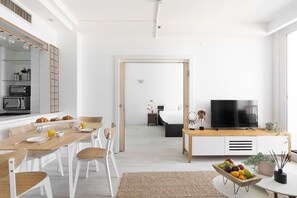 Uma sala moderna com espaço de jantar, TV e cozinha visível por uma porta aberta.