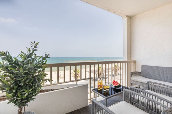 Un balcon donnant sur la plage, des meubles en osier et une plante en pot.