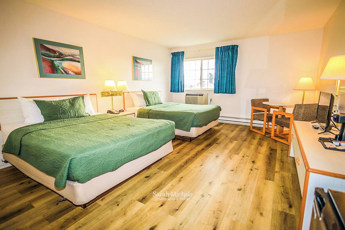 A hotel room with two beds, a desk with a computer, a chair, and a window with curtains.