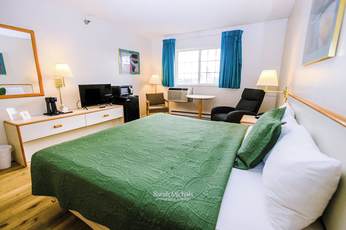 A hotel room with a bed, desk, chair, and a TV.
