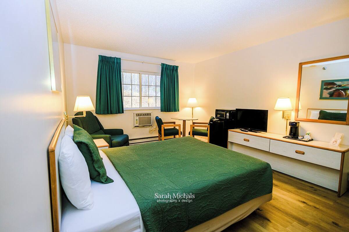A hotel room with a bed, a desk, a chair, a television, and a coffee maker.
