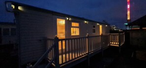 A small, single-story building with a wooden deck and a lit interior. - Staycation Opposite Fantasy Island Ingoldmells (Skegness)