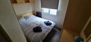 A small, narrow room with a single bed, a window with a blind, and a small table with a chair. - Staycation Opposite Fantasy Island Ingoldmells (Skegness)