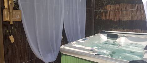 A hot tub with a control panel, surrounded by a bamboo fence and a white curtain.