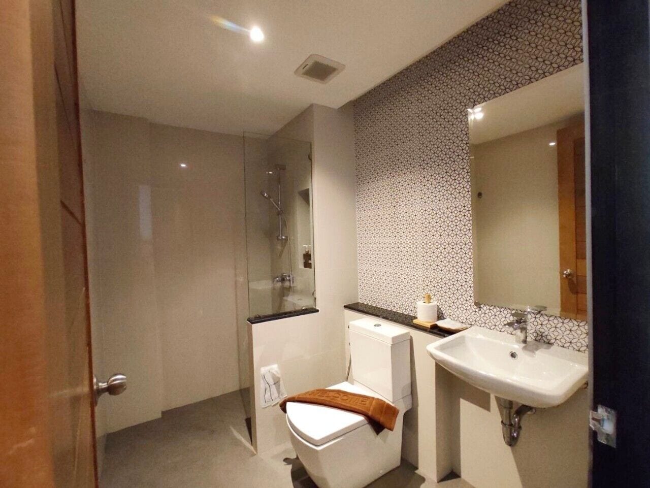 Un baño moderno con cabina de ducha de vidrio, inodoro y lavamanos con espejo.