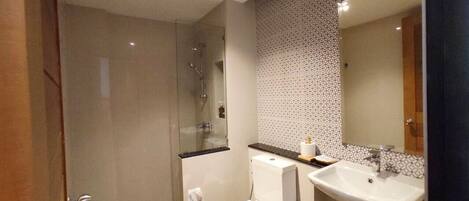 Un baño moderno con cabina de ducha de vidrio, inodoro y lavamanos con espejo.