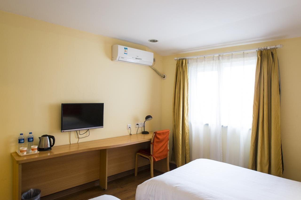 Ein Hotelzimmer mit Bett, Schreibtisch mit Fernseher, Stuhl und einem Fenster mit Vorhängen.