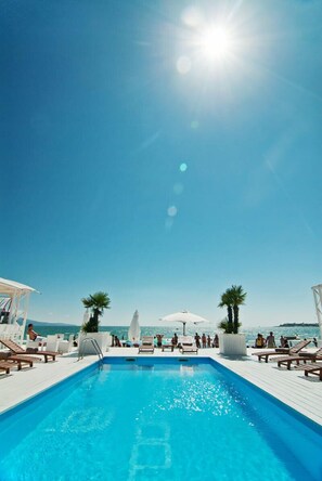 A clear blue sky, a swimming pool with lounge chairs, and palm trees. - Hotel Amfibia Beach (Sunny Beach)