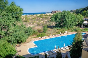 A swimming pool with lounge chairs and umbrellas, surrounded by greenery and a view of the sea. - Hotel Amfibia Beach (Sunny Beach)