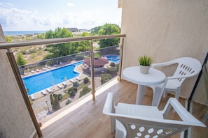 A balcony with a pool view, white plastic chairs, and a small table with a plant. - Hotel Amfibia Beach (Sunny Beach)