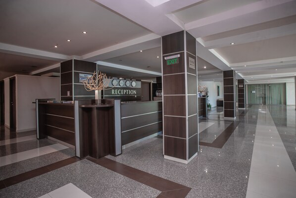 A modern reception area with a reception desk, a clock, and a sign indicating an exit. - Hotel Amfibia Beach (Sunny Beach)