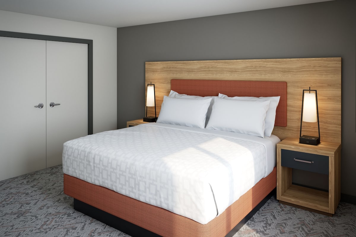 A modern hotel room with a large bed, wooden headboard, two bedside tables with lamps, and a wardrobe.