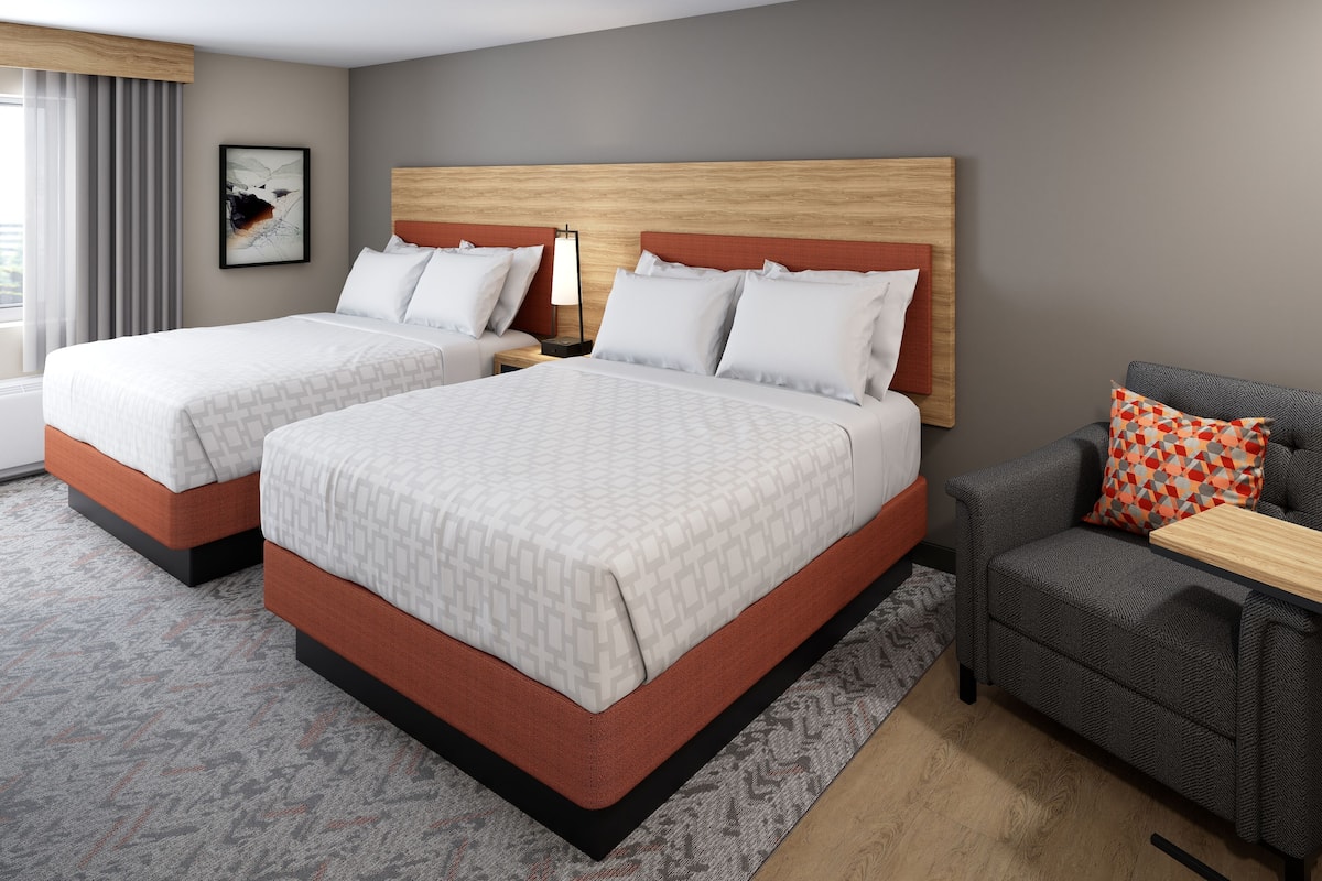 A hotel room with two beds, a sofa, a nightstand, and a wall-mounted lamp.