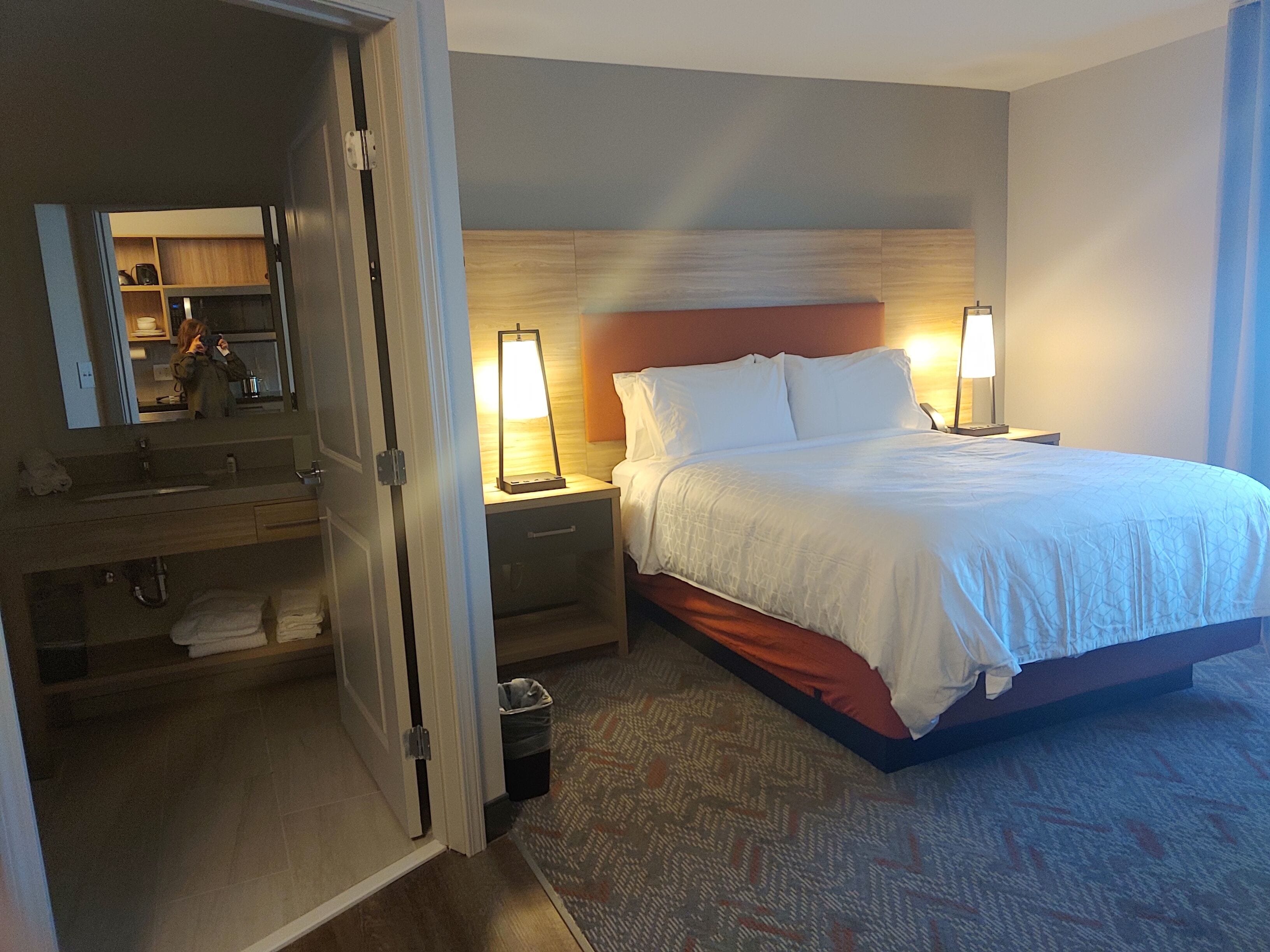 Quarto de hotel com cama, mesas de cabeceira, espelho e banheiro visível por uma porta aberta.