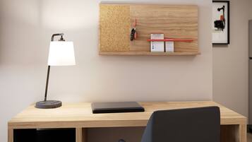 A modern office desk with a laptop, a desk lamp, a corkboard with keys and a sign, and a framed picture on the wall.