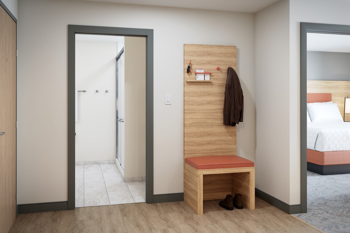 Een hotelkamer met een houten bankje, een kapstok en een bed met hoofdeinde.