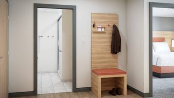 Habitación de hotel con un banco de madera, un perchero y una cama con cabecera.