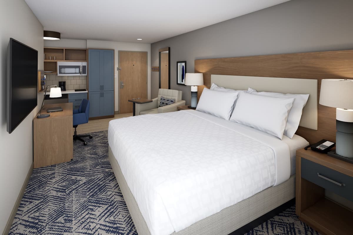 A hotel room with a large bed, a desk, a chair, a microwave, and a kitchenette.