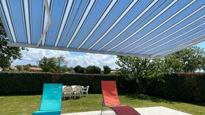 A covered patio area with two lounge chairs, one blue and one red, and a table with chairs.