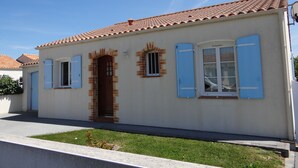 A single-story building with a tiled roof, a central entrance with a wooden door, and two windows with blue shutters.