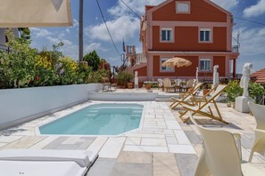 Un área de piscina con sillones de descanso, una piscina pequeña y un edificio con balcones al fondo.