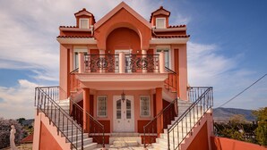 Ein zweistöckiges Gebäude mit einem zentralen Eingang, einem Balkon mit aufwendiger Balustrade und einer Treppe, die zum Eingang führt.