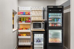 A compact kitchenette with a microwave, mini-fridge, and pantry shelves stocked with snacks and beverages. - Spark by Hilton Dothan (Dothan)