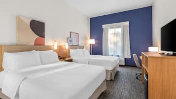A hotel room with two beds, a desk, a chair, a television, and a window with curtains.