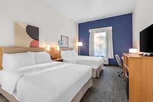 Una camera d'albergo con due letti, una scrivania, una sedia, una televisione e una finestra con tende.