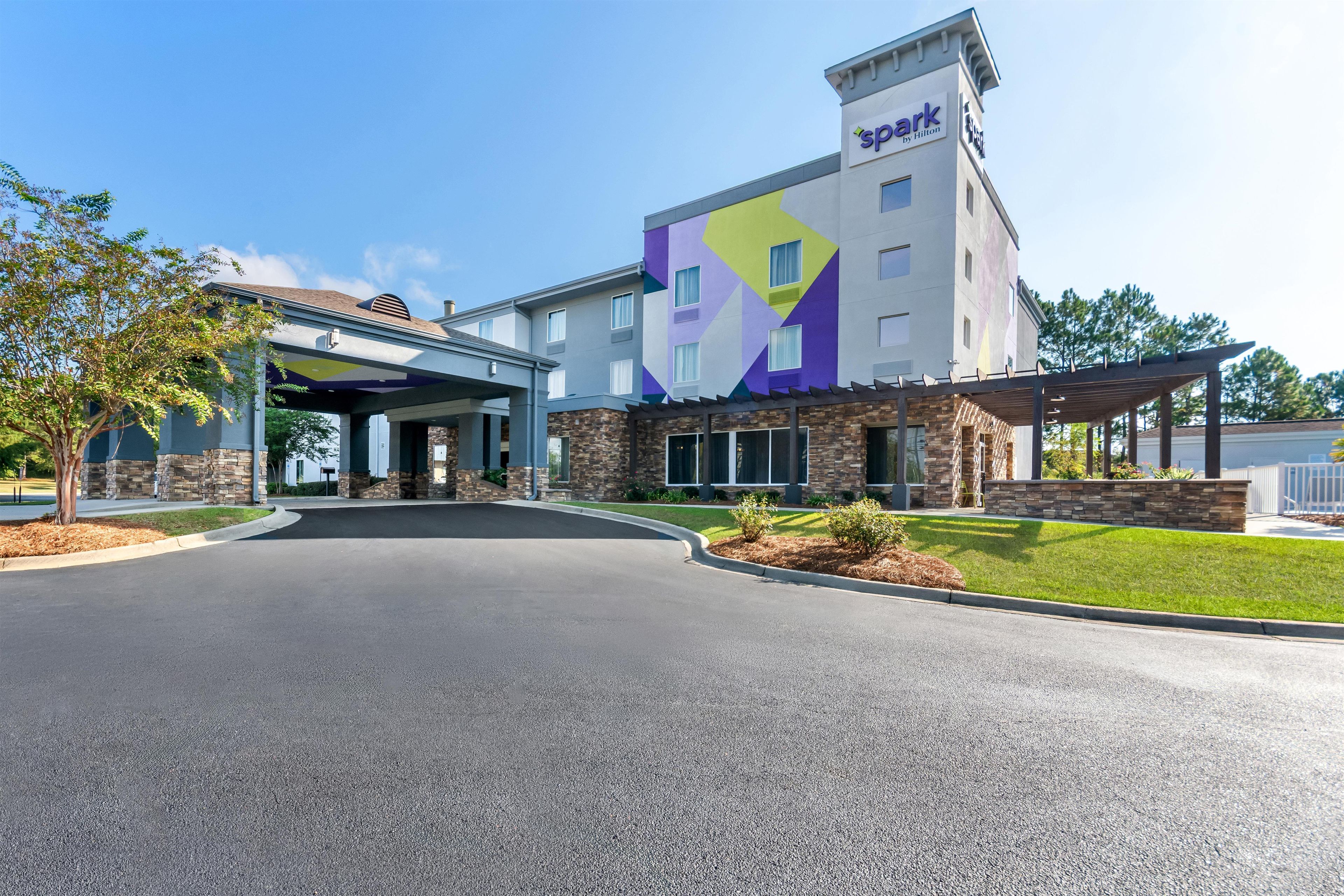 A hotel with a modern design, featuring a prominent 'Spark by Hilton' sign, a covered entrance, and a well-maintained lawn.