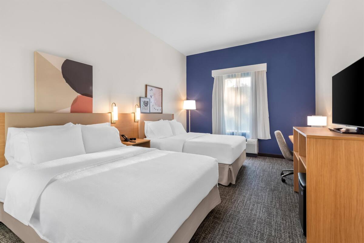 A hotel room with two beds, a desk, a chair, a television, and a window with curtains.