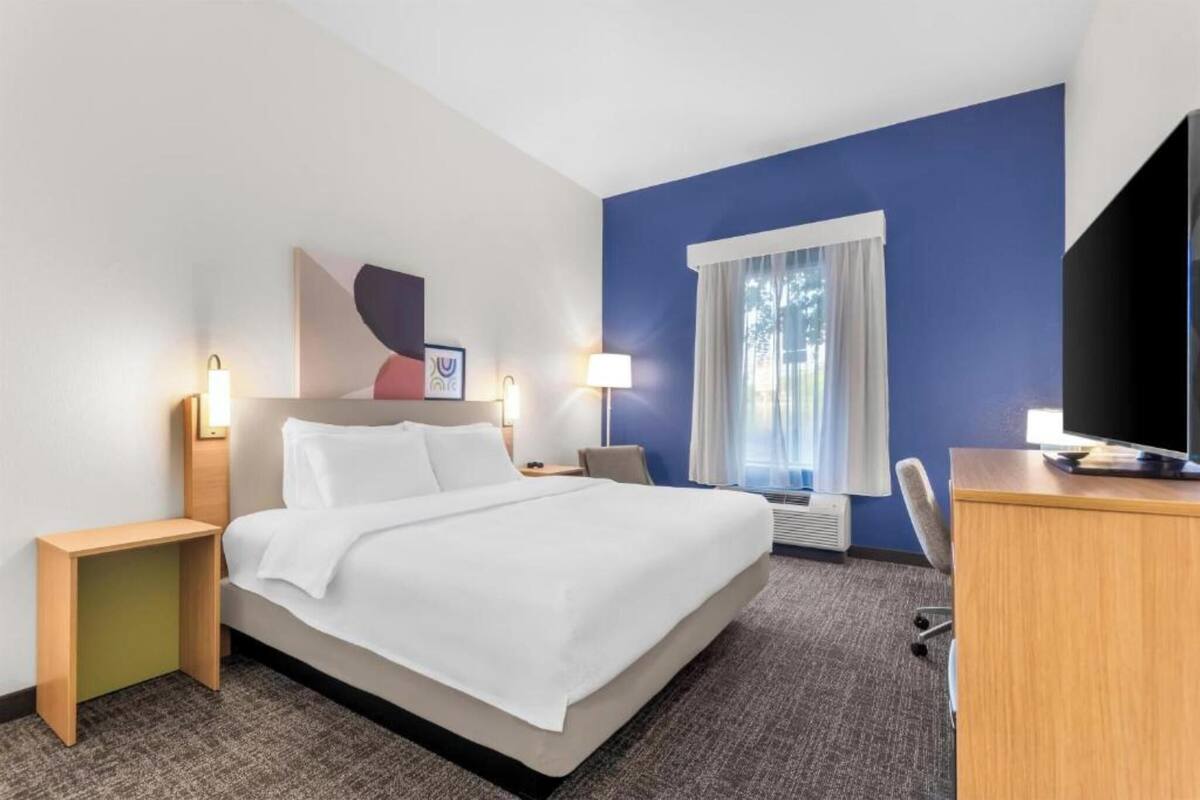 A hotel room with a bed, bedside tables, a desk, a chair, a television, and a window with curtains.