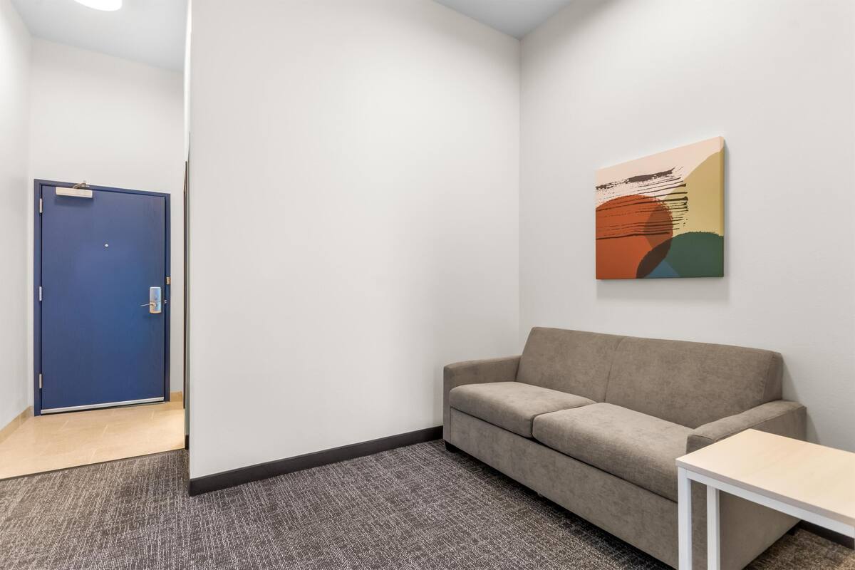 A room with a blue door, a beige sofa, a small white table, and a colorful abstract painting on the wall.