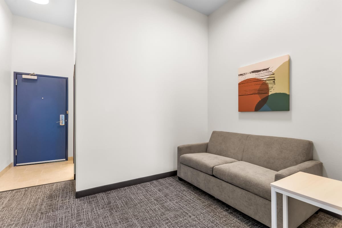 Una habitación con una puerta azul, un sofá color beige, una mesita blanca pequeña y un cuadro abstracto de colores en la pared.