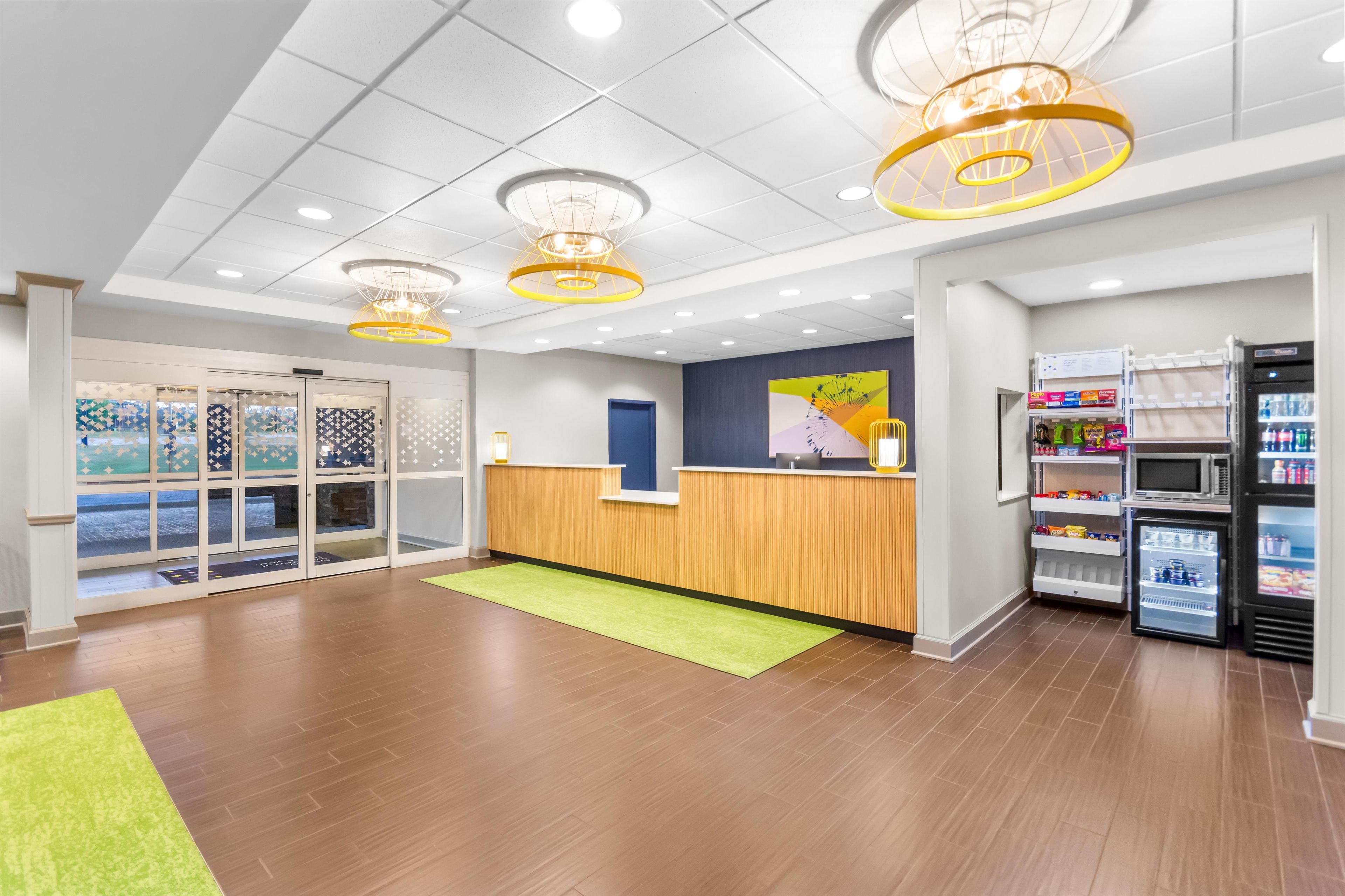 A reception area with a wooden counter, a green rug, and a refrigerator stocked with beverages.
