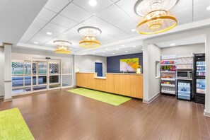 A reception area with a wooden counter, a green rug, and a refrigerator stocked with beverages. - Spark by Hilton Dothan (Dothan)