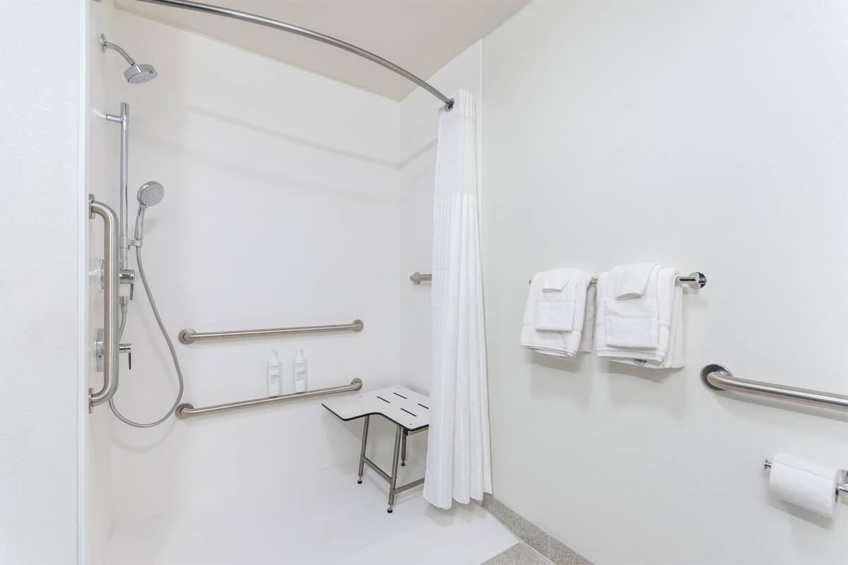 A modern bathroom with a shower, grab bars, a bench, and a toilet paper holder.