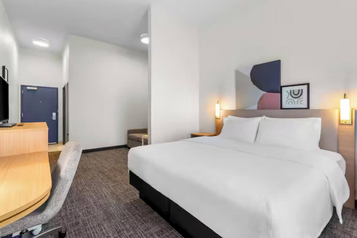 A hotel room with a bed, a desk, a chair, and a reception area.