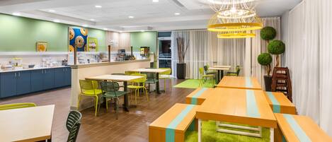 A modern hotel lobby with a counter, seating area, and a large chandelier.