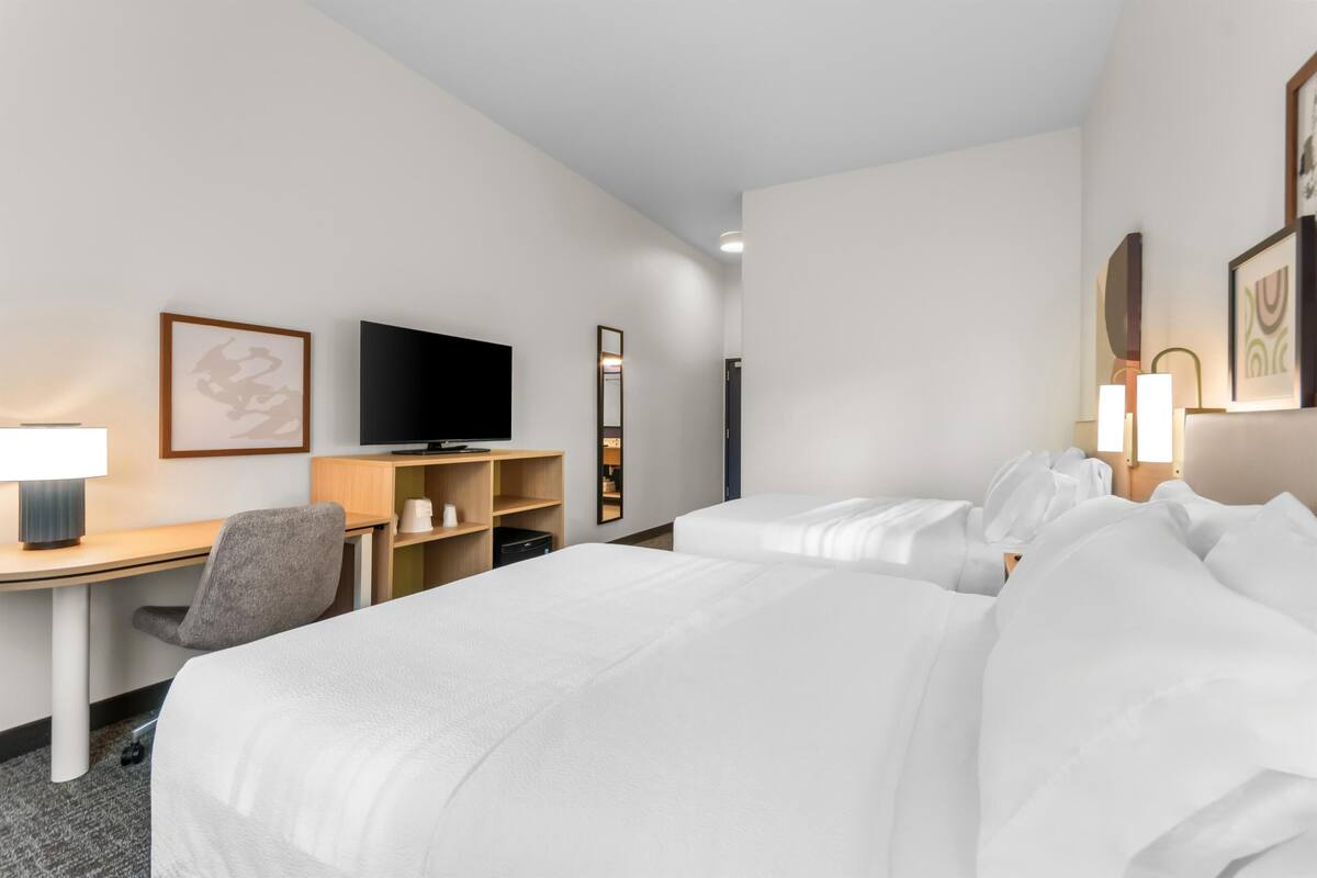 A hotel room with a desk, two beds, a television, and framed artwork on the walls.