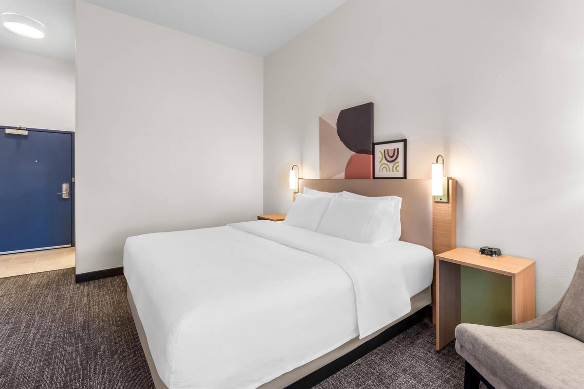 A hotel room with a bed, a nightstand, a chair, and a door.